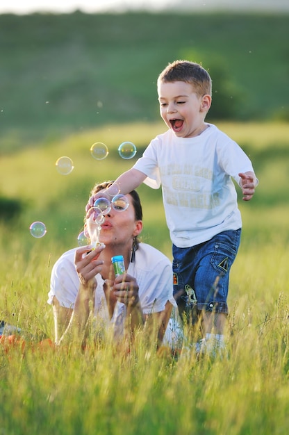 enfant heureux et femme jouant en plein air avec une bulle de savon sur le pré