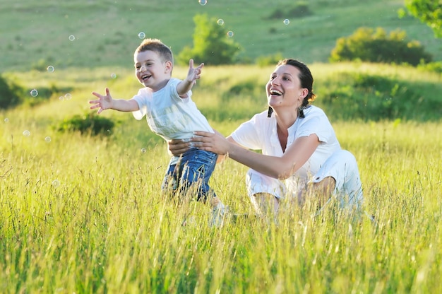 enfant heureux et femme jouant en plein air avec une bulle de savon sur le pré