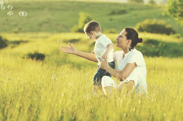 enfant heureux et femme jouant en plein air avec une bulle de savon sur le pré