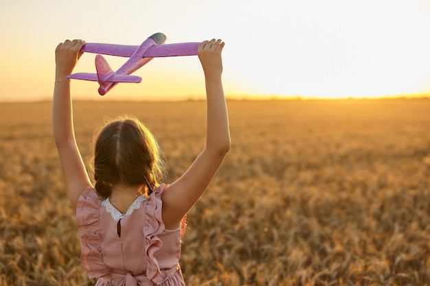 Enfant heureux, fille jouant avec l'avion jouet sur le champ de blé d'été