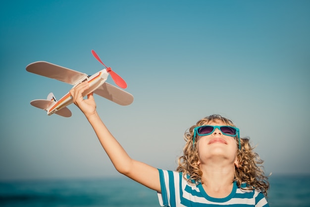 enfant heureux jouant avec un avion jouet contre la mer et le ciel en vacances d'été