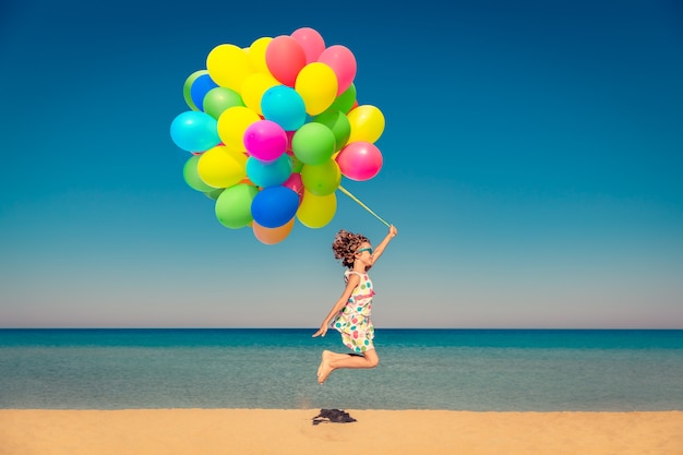 Enfant heureux jouant avec des ballons multicolores lumineux en vacances d'été Enfant s'amusant sur la plage contre la mer et le ciel bleus