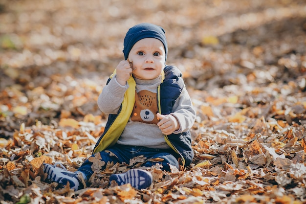 Enfant heureux jouant dans un tas de feuilles pendant l'automne. Mignon petit bébé dans le parc automne avec des feuilles jaunes