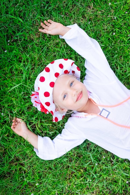 Un enfant heureux et joyeux une fille se trouve sur l'herbe verte de la pelouse et un chapeau panama en été et sourit