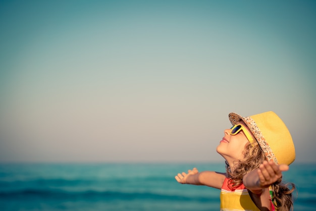 enfant heureux avec les mains ouvertes contre la mer et le ciel bleus