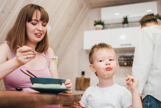 Un enfant heureux mange des pâtes dans la cuisine avec sa famille