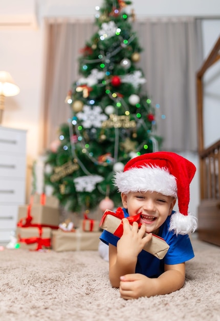 Un enfant heureux le matin de Noël reçoit un cadeau posé sur un tapis confortable dans sa chambre en pyjama