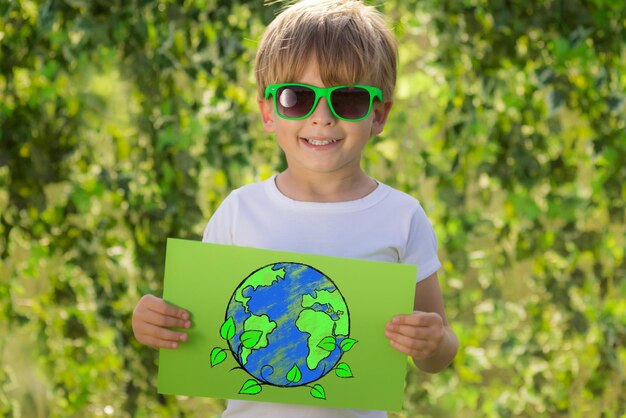 Enfant heureux montrant du papier avec une planète dessinée. Portrait d'enfant en plein air. Garçon sur fond de printemps vert flou. Jour de la terre et concept d'écologie