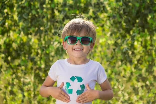 Enfant heureux montrant le signe de recyclage. Portrait d'enfant en plein air. Garçon sur fond de printemps vert flou. Jour de la terre et concept d'écologie