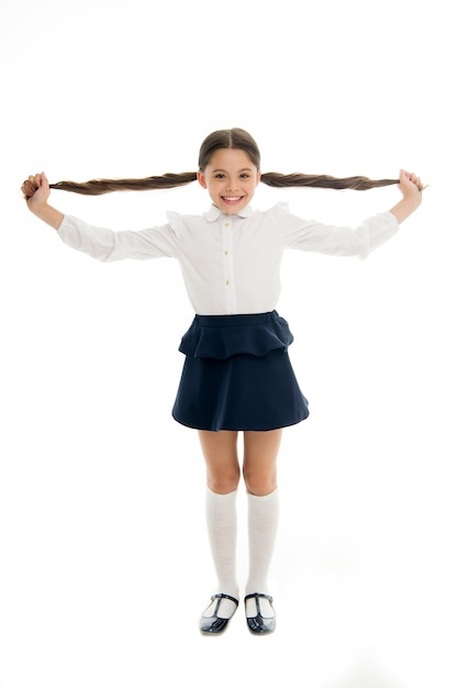 Enfant heureux montre de longs cheveux bruns isolés sur blanc. Sourire de fille de mode avec une nouvelle coiffure. Fier de ses beaux cheveux. Services de salon de coiffure pour petite fille. Salon de beauté. Élégant et mignon.