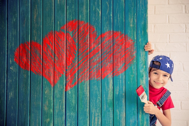 Enfant heureux peignant un grand coeur rouge sur le mur. Fille drôle jouant à la maison. Carte de Saint Valentin. Concept de rénovation et de design