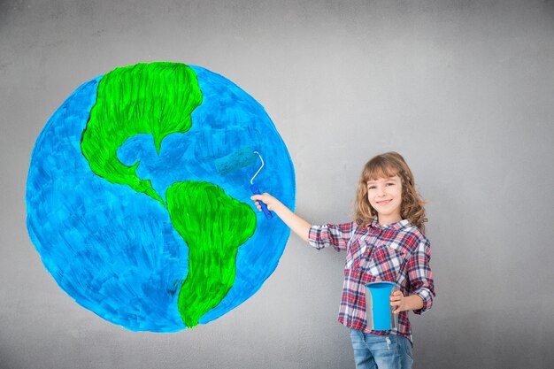 Enfant heureux peignant le mur avec la couleur bleue. Enfant s'amusant à la maison. Concept de rénovation de printemps