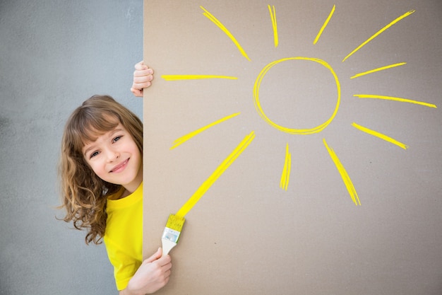 enfant heureux peignant un soleil jaune sur le mur