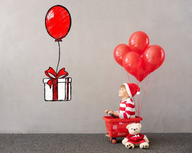 Enfant heureux portant le costume de Noël Enfant assis dans un panier avec des ballons rouges