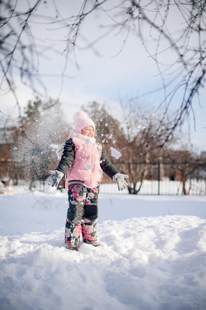 Un enfant heureux en promenade hivernale, une petite fille en costume chaud, joue dans l'arrière-cour et profite d'une journée ensoleillée en hiver...