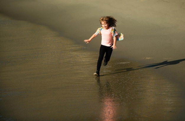 Un enfant heureux qui court sur la plage, un garçon drôle qui court le long du bord du surf, un enfant actif, un petit coureur.