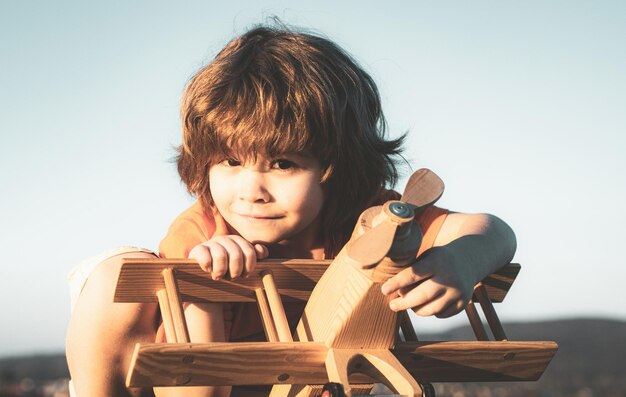 Un enfant heureux rêve de voyager et de jouer avec un avion jouet Petit aviateur pilote en plein air sur fond bleu ciel d'été Rêves d'enfant