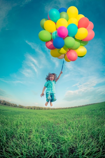 Enfant heureux sautant avec des ballons jouets colorés à l'extérieur Enfant souriant s'amusant dans un champ de printemps vert sur fond de ciel bleu Concept de liberté