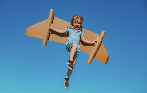 Enfant heureux sautant et jouant avec des ailes de jouet sur fond de ciel d'été