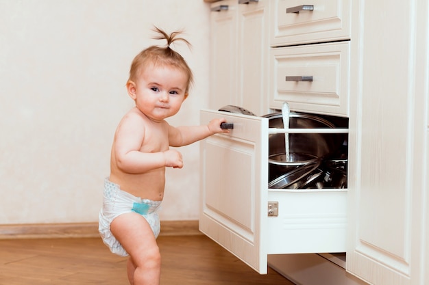 Un enfant heureux se tient près d'un placard ouvert dans la cuisine. enfant dans la cuisine blanche. enfant sourit dans une cuisine blanche.