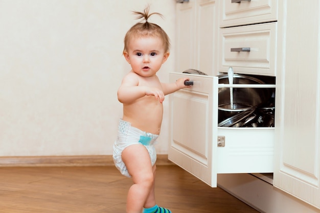 Un enfant heureux se tient près d'un placard ouvert dans la cuisine. enfant dans la cuisine blanche. enfant sourit dans une cuisine blanche.