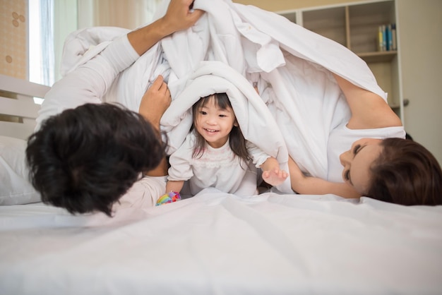 Photo un enfant heureux avec ses parents jouant dans le lit à la maison.