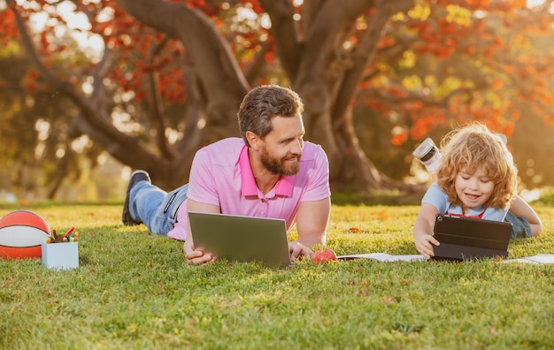 Enfant heureux avec son père apprenant en plein air en étudiant en ligne et en travaillant sur un ordinateur portable dans un champ vert