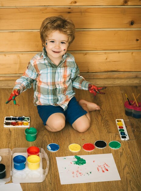 Enfant heureux souriant avec des mains colorées, des peintures à la gouache et des dessins