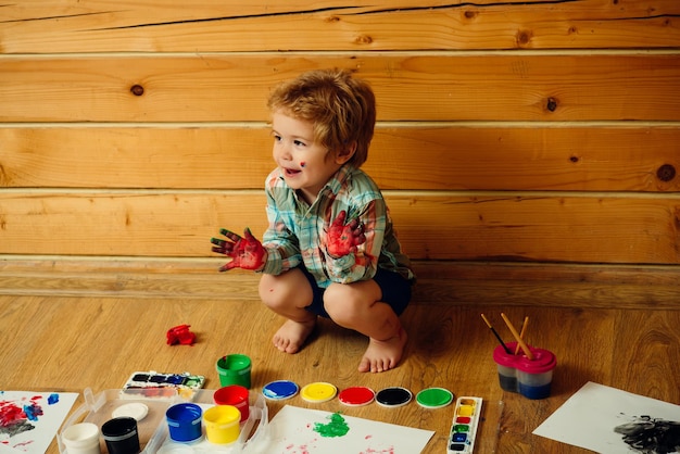 Enfant heureux souriant avec des mains colorées, des peintures à la gouache et des dessins