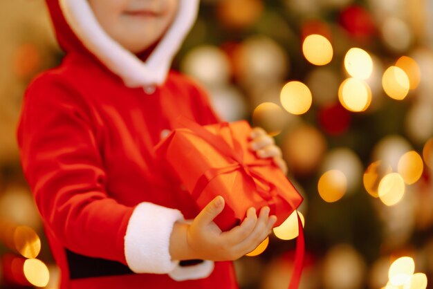 Enfant heureux tenant une boîte cadeau rouge sur les lumières de fond.