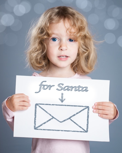 Enfant heureux tenant une carte de Noël avec une lettre dessinée à la main pour le père Noël et un cadeau