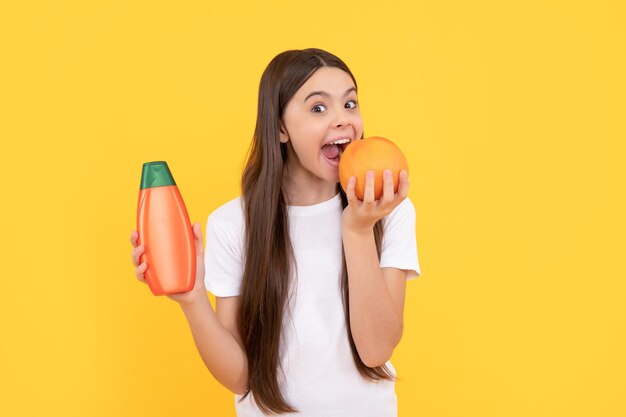 Un enfant heureux tient une bouteille de shampoing et mange du pamplemousse sur fond jaune vitamine