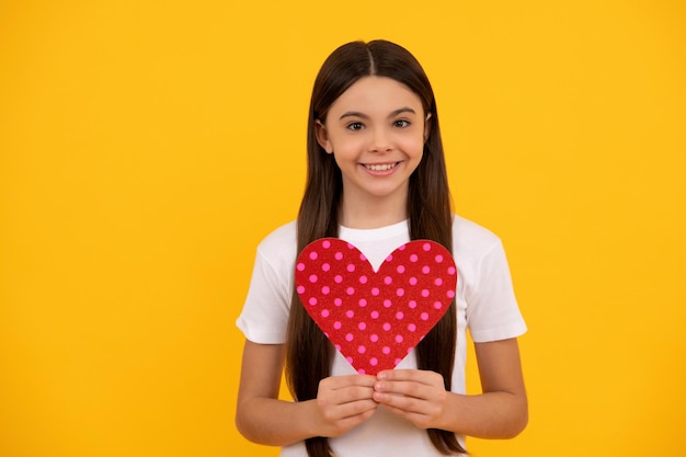 Un enfant heureux tient un coeur d'amour sur fond jaune, saint valentin.