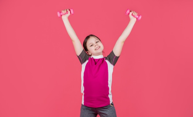 Un enfant heureux tient des haltères de fitness sur fond rose