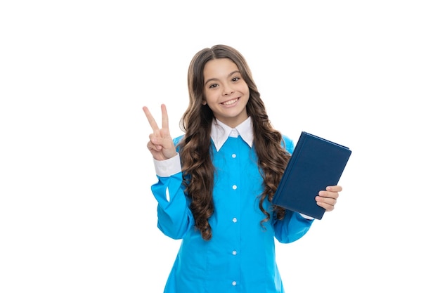 Un enfant heureux tient un livre scolaire montrant le signal de la main V isolé sur la paix blanche