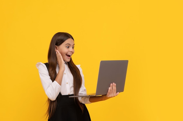 Un enfant heureux en uniforme scolaire étudie sur un ordinateur portable, éducation en ligne.