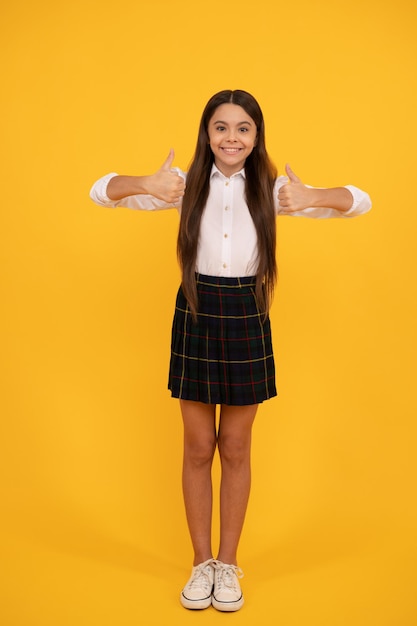 Enfant heureux en uniforme scolaire pleine longueur montrant les pouces vers le haut sur fond jaune émotions positives