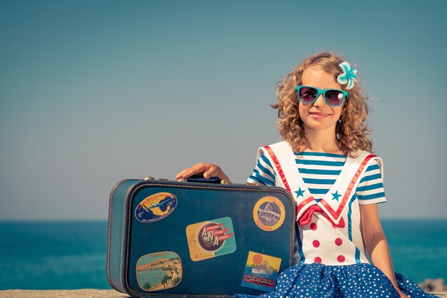 Enfant heureux avec valise sur la plage L'enfant profite de vacances d'été à la mer Concept de voyage et de vacances