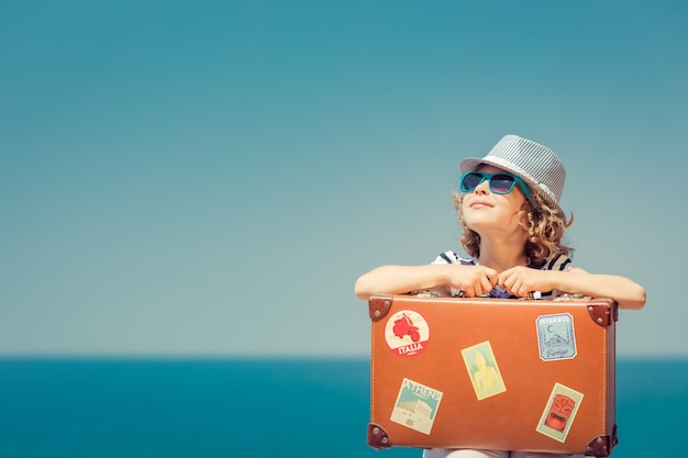 Enfant heureux avec valise sur la plage L'enfant profite de vacances d'été à la mer Concept de voyage et de vacances