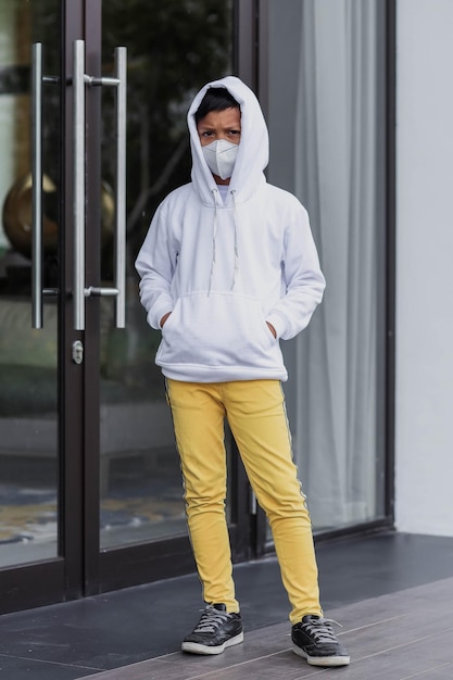 Enfant hipster portant un sweat à capuche blanc uni et un masque de protection pour une maquette de sweat à capuche