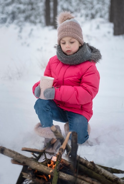 Enfant en hiver. Petite fille en hiver dans la nature, boire du thé au coin du feu