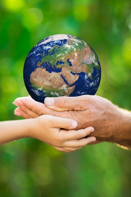 Enfant et homme âgé tenant la Terre dans les mains sur fond de printemps vert Éléments de cette image fournis par la NASA