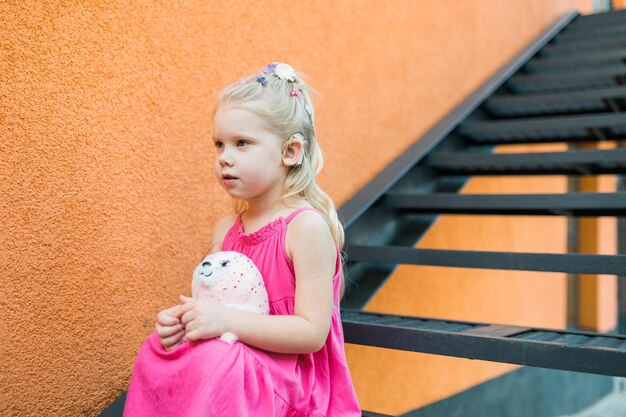 Une enfant avec un implant cochléaire d'aide auditive dans une robe rose s'amusant sur l'aide de rue d'été pour le