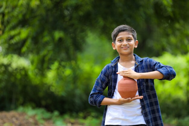 Enfant indien mignon tenant la tirelire d'argile dans la main