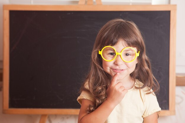 Un enfant intelligent portant des lunettes jaunes se tenait devant un tableau noir