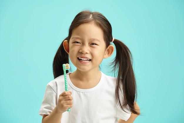 Une enfant japonaise avec deux queues de cheval tenant une brosse à dents et souriante heureuse préparant la brosse elle-même