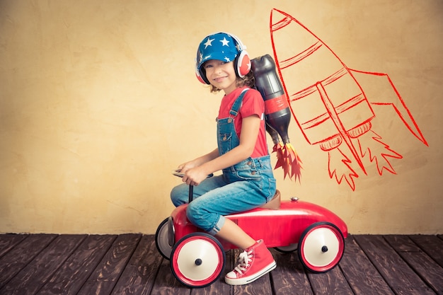 Enfant avec jet pack conduisant une voiture jouet rétro. Enfant jouant à la maison. Concept de succès, de leader et de gagnant