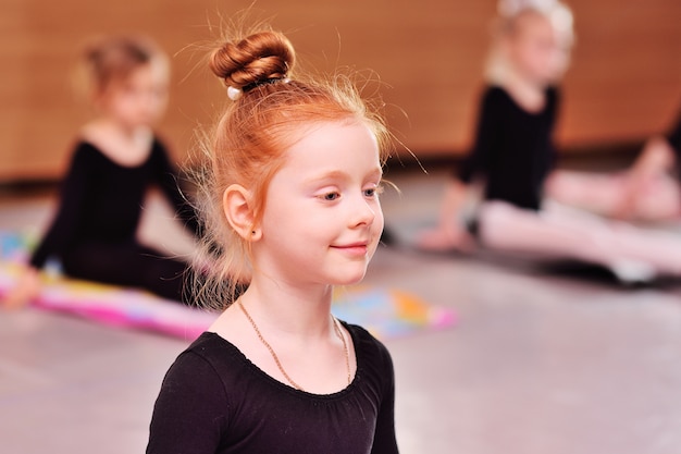 Enfant - la jolie ballerine rousse effectue des exercices d&#39;étirement à l&#39;école de ballet