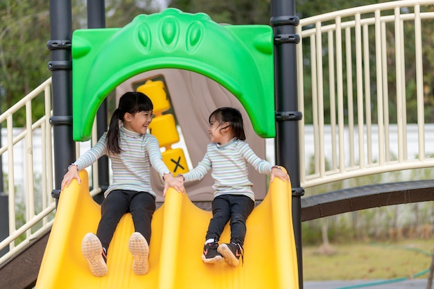 Enfant jouant sur une aire de jeux extérieure. Les enfants jouent dans la cour de l'école ou de la maternelle. Enfant actif sur un toboggan coloré et une balançoire. Activité estivale saine pour les enfants.