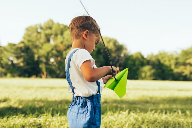 Enfant jouant avec un avion en papier en journée d'été dans le parc Petit garçon jouant à des jeux de plein air sur l'herbe verte Concept de l'enfance